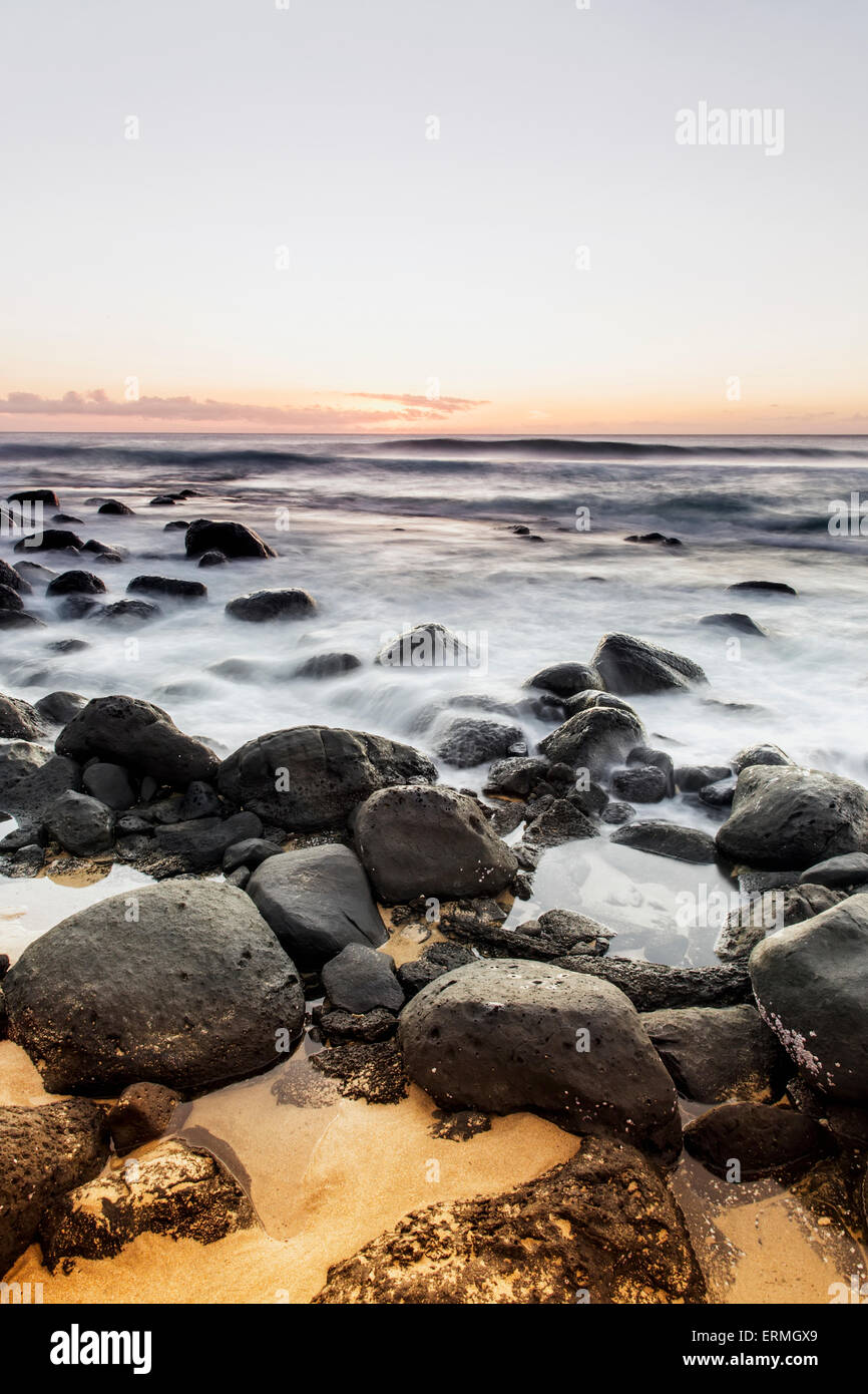 Lavaggio ad acqua su rocce lungo la riva al tramonto; Wainiha, Kauai, Hawaii, Stati Uniti d'America Foto Stock