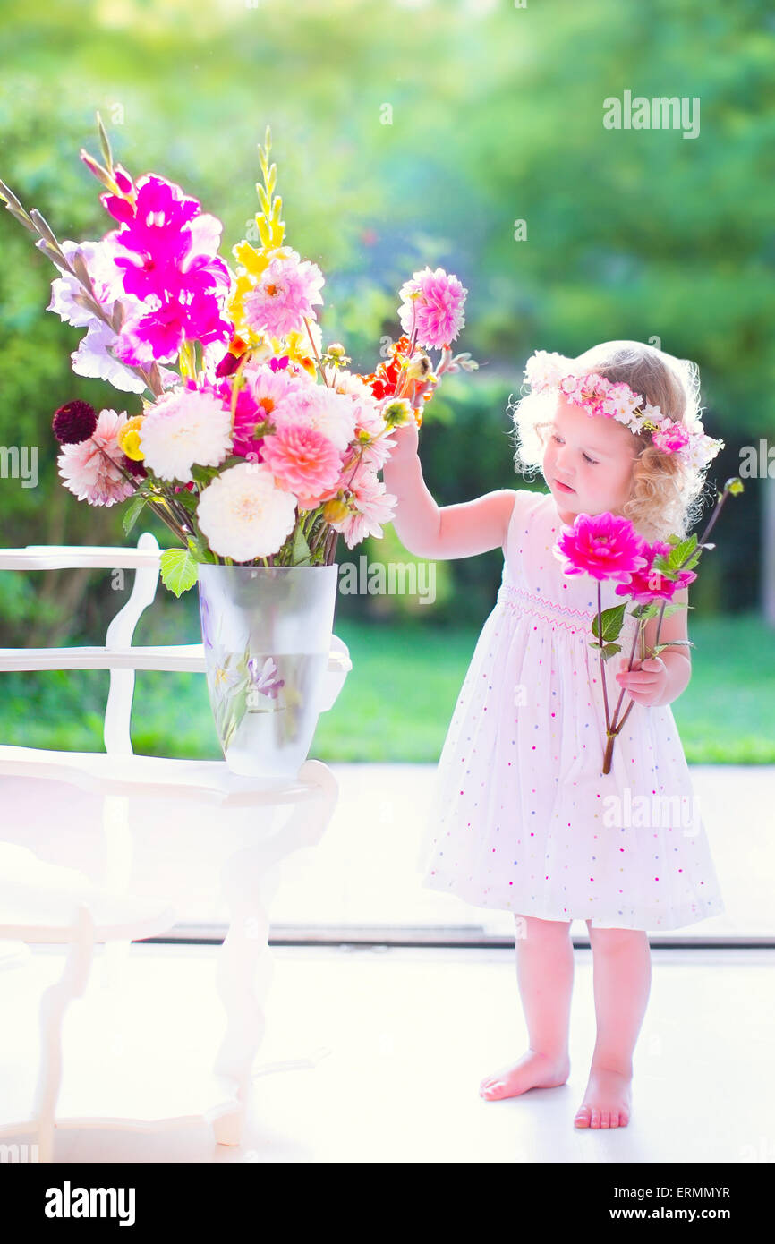 Bella ragazza con i capelli ricci che indossa un abito bianco fiori profumati e colorati di mazzo di fiori in un vaso grande Foto Stock