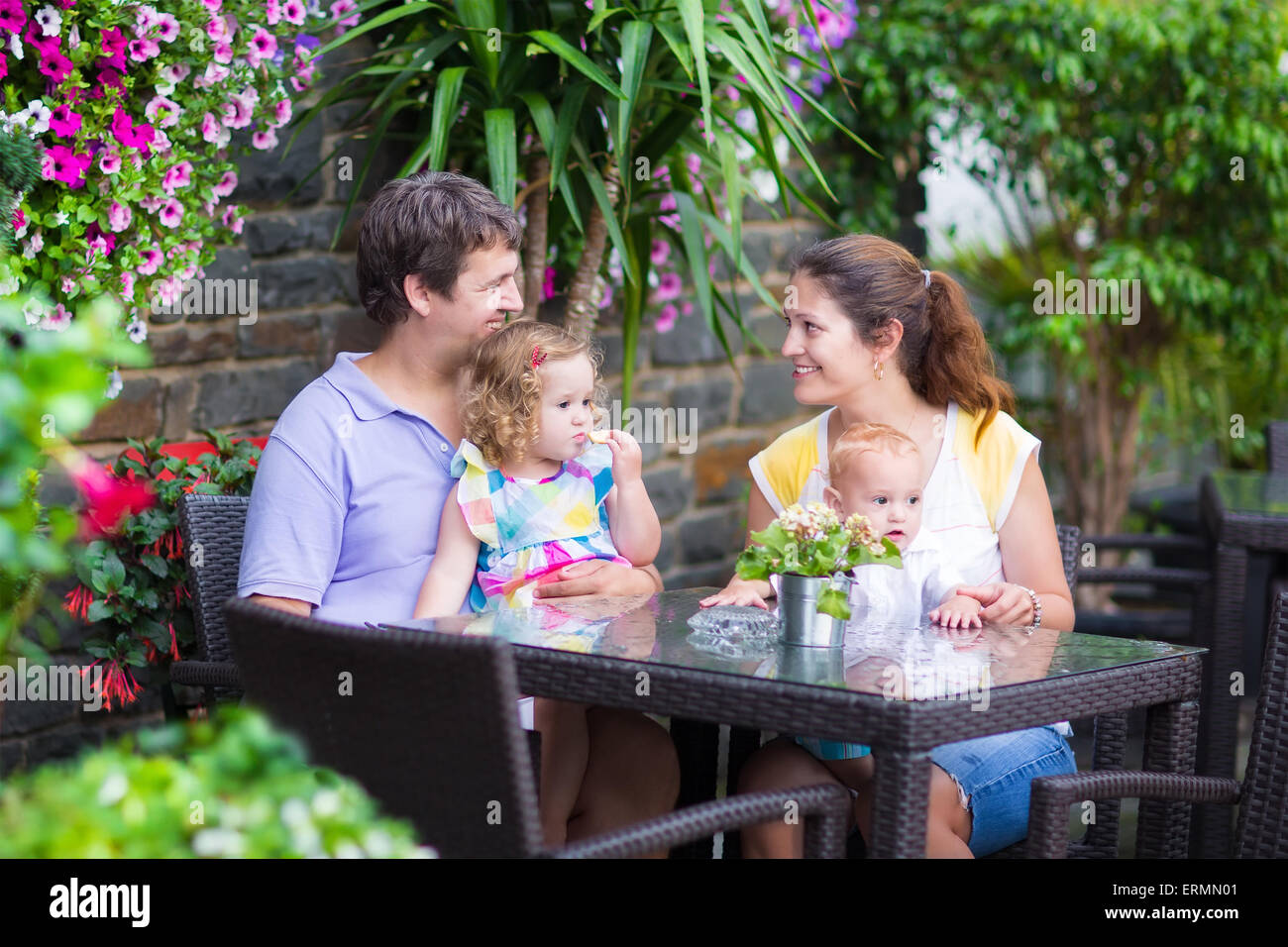 Felice famiglia giovane, genitori con due bambini a mangiare il pranzo in una bellissima outdoor cafe con fiori in una città Foto Stock