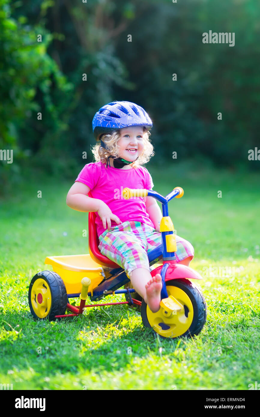 Carino divertente toddler girl cavalcare la sua bicicletta che indossa un casco di sicurezza godendo di una bella giornata di sole in un giardino estivo a giocare all'aperto Foto Stock