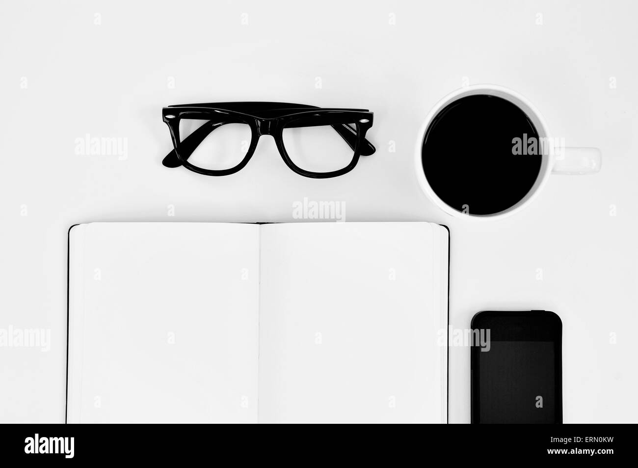 Alta angolazione di un fustellato notebook, una coppia di plastica nera cerchiati di occhiali, una tazza di caffè e un smartphone su un bianco tabl Foto Stock