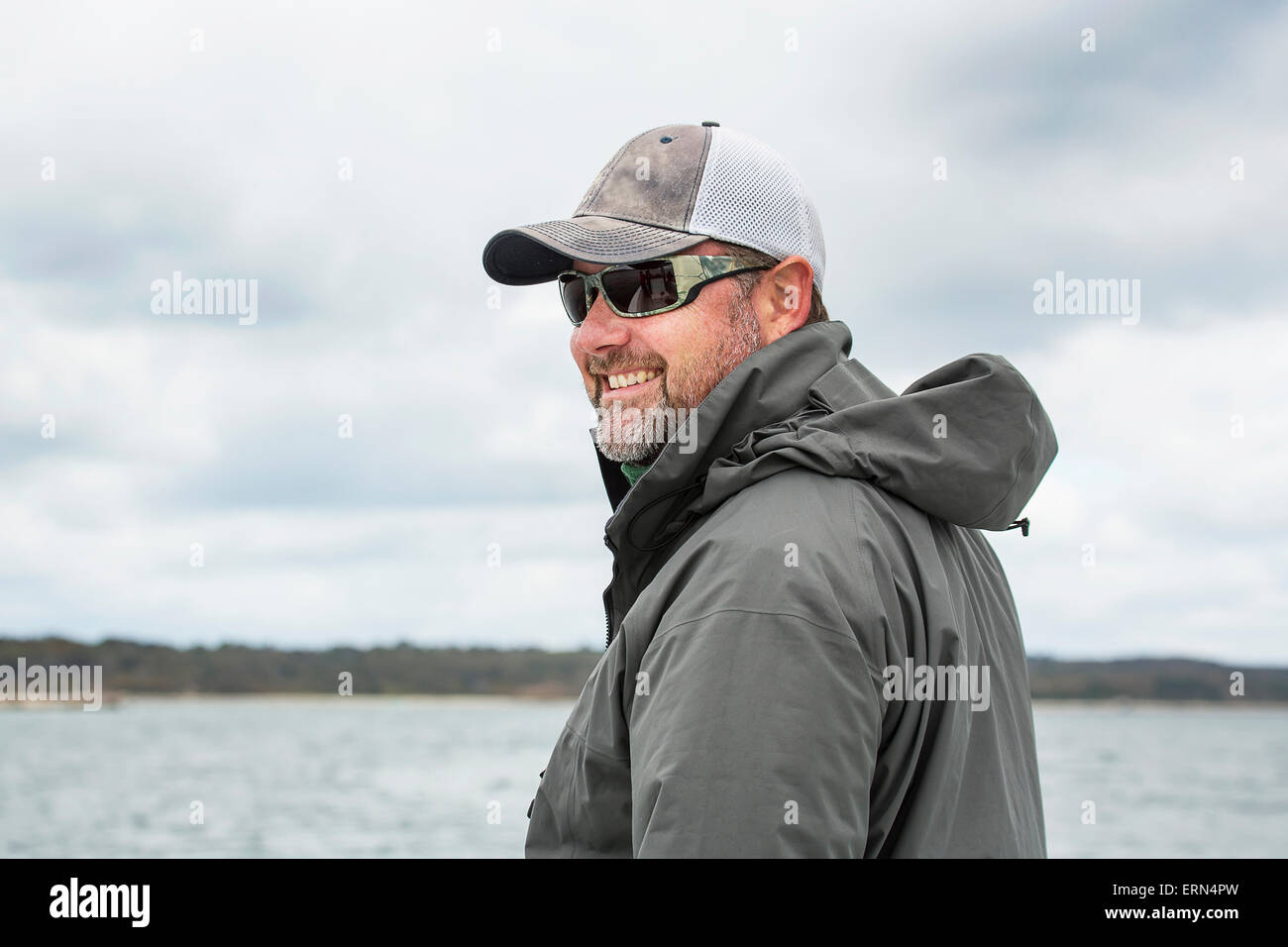 Un uomo che indossa gli occhiali da sole e un cappello sorge su una barca da pesca con una vista dell'acqua e le coste; Maine, Stati Uniti d'America Foto Stock