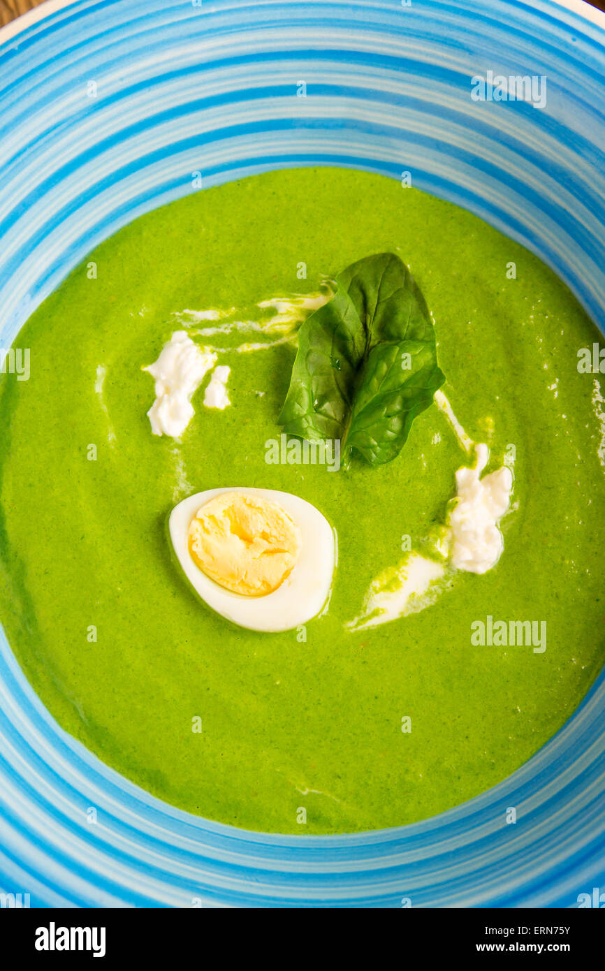 Verde di spinaci minestra in crema con uovo e panna acida su blu tavolo in legno Foto Stock
