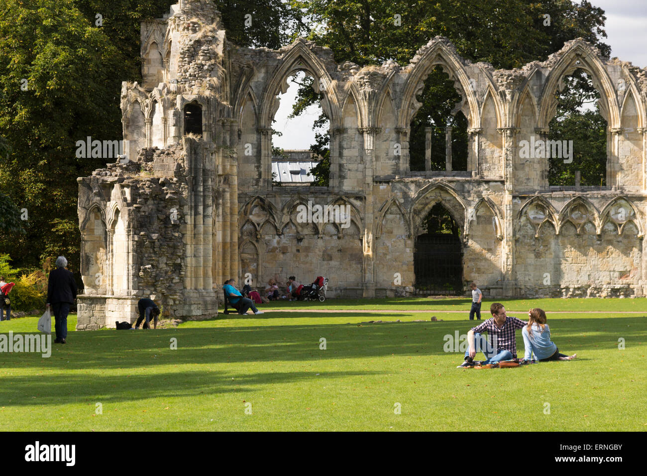 Persone sedute e a piedi, godendo i Giardini del Museo sotto il sole estivo, dal grado i elencato St Mary's Abbey a York, Yorkshire, Regno Unito Foto Stock