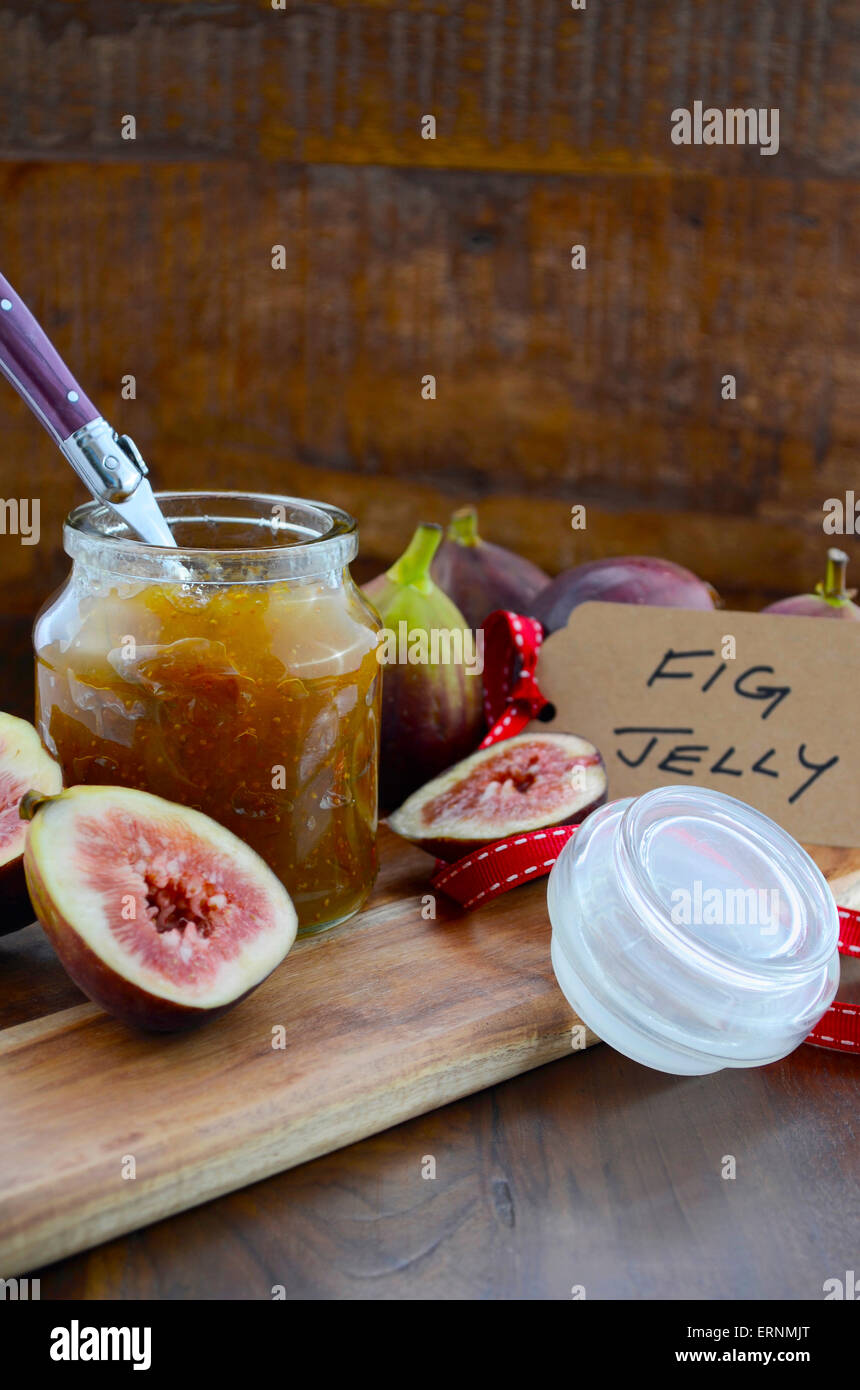 Fresche e mature frutto autunnale, fichi, con fig jelly preservare in vaso sul bordo di taglio contro il legno scuro dello sfondo. Foto Stock