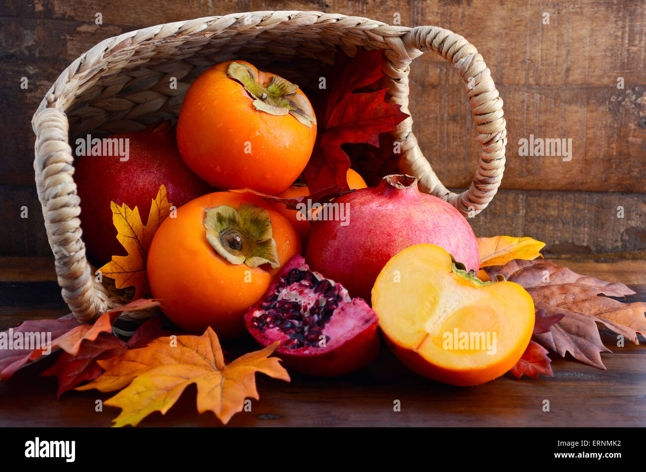 Cesto di fresche cachi e melograni con tagliare a fette in autunno cadono le foglie contro un legno scuro dello sfondo vintage. Foto Stock