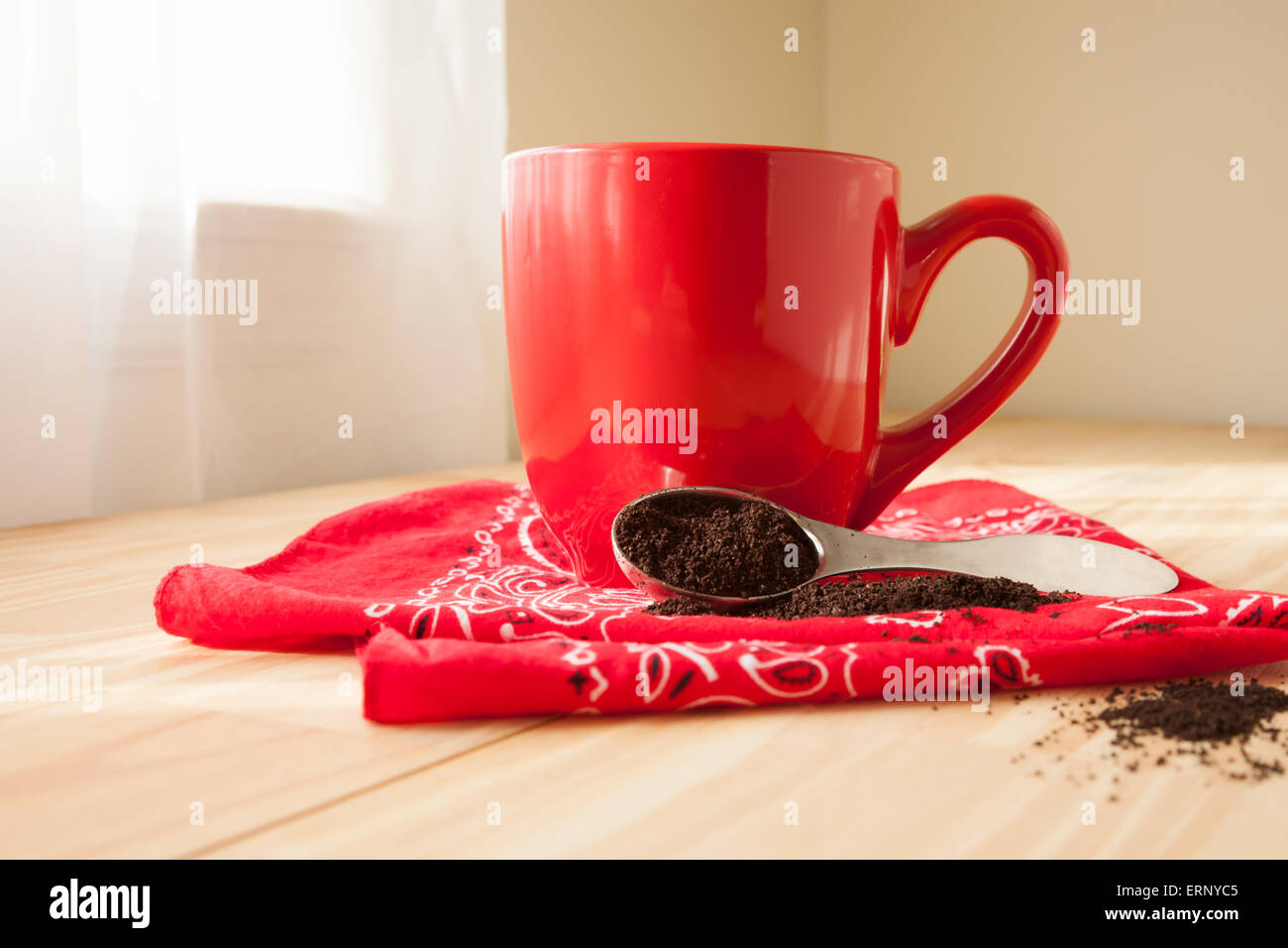 Un rosso tazza da caffè si trova sulla cima di un rosso bandana igienico. Un cucchiaio di caffè macinato viene versato intorno e si siede accanto alla tazza. Foto Stock