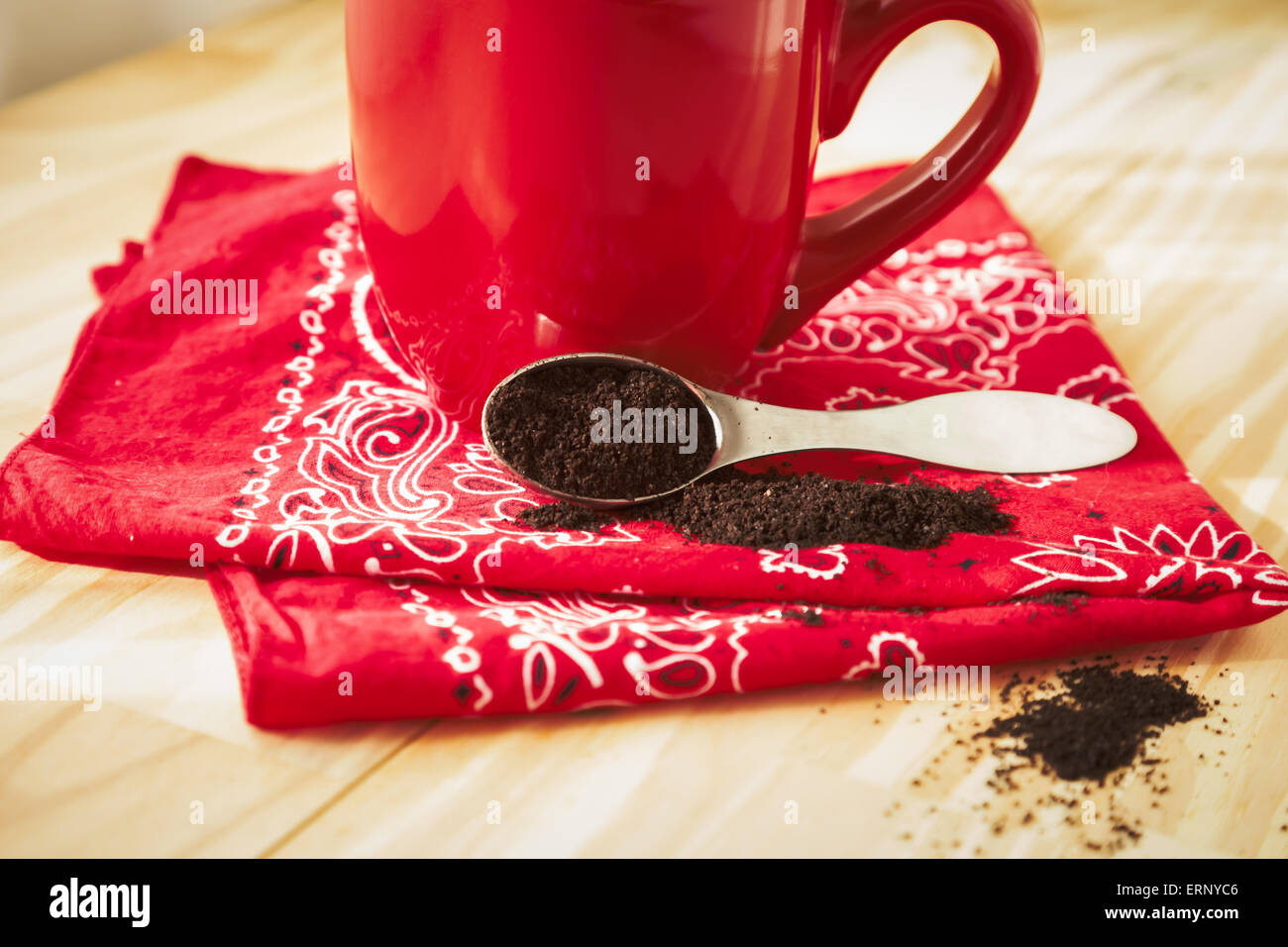 Un rosso tazza da caffè si trova sulla cima di un rosso bandana igienico. Un cucchiaio di caffè macinato viene versato intorno e si siede accanto alla tazza. Foto Stock