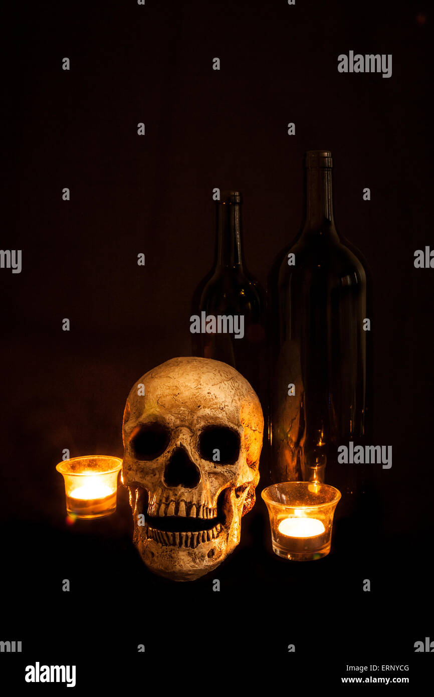 Un cranio vintage si siede accanto a due bottiglie di vino; immagine illuminato a lume di candela e usando una luce tecnica di pittura. Foto Stock