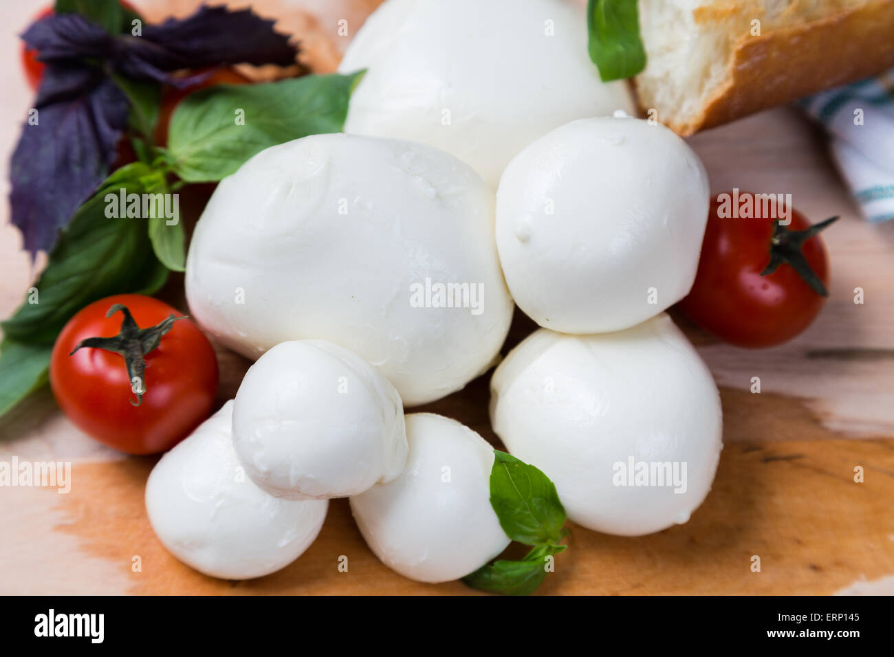 Mozzarella di sfere di dimensioni diverse con pomodori ciliegia, pane e basilico su sfondo di legno Foto Stock