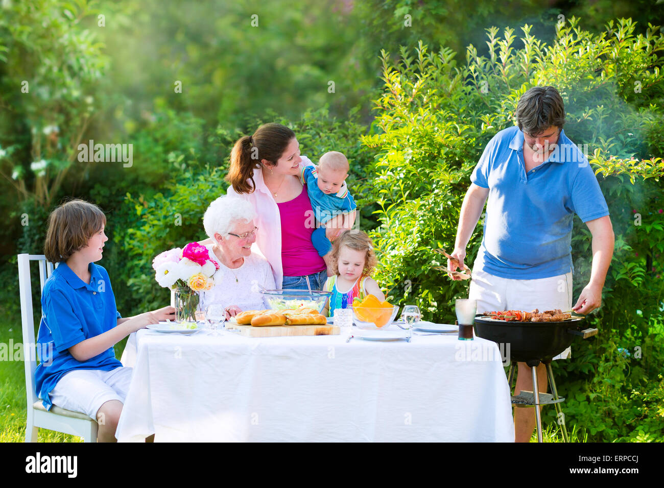 Grill barbecue party nel cortile. Felice famiglia grande godendo di pranzo a barbecue con la nonna di mangiare carne nel giardino con insalata Foto Stock