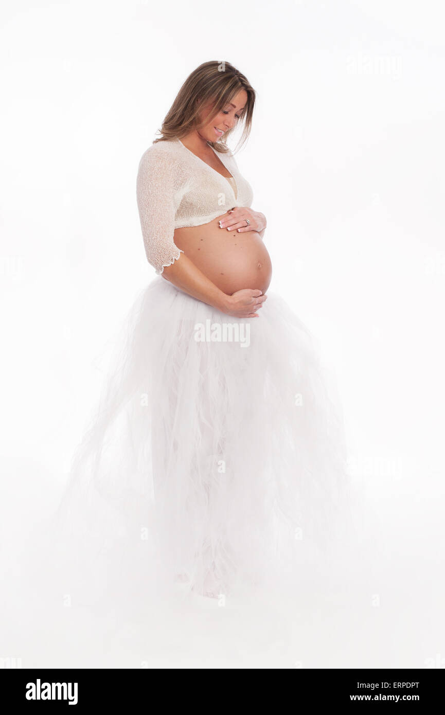 Ritratto di una bella donna incinta indossando un bianco a piena lunghezza tutu. Lei è sempre sorridente e guardando verso il basso al suo ventre. Isolato Foto Stock