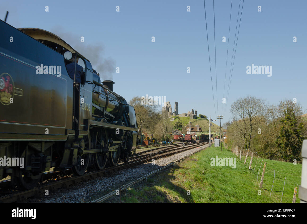 Treno a vapore che arrivano alla stazione di Corfe. Corfe Castle in background. Dorset, Regno Unito. Aprile. Foto Stock