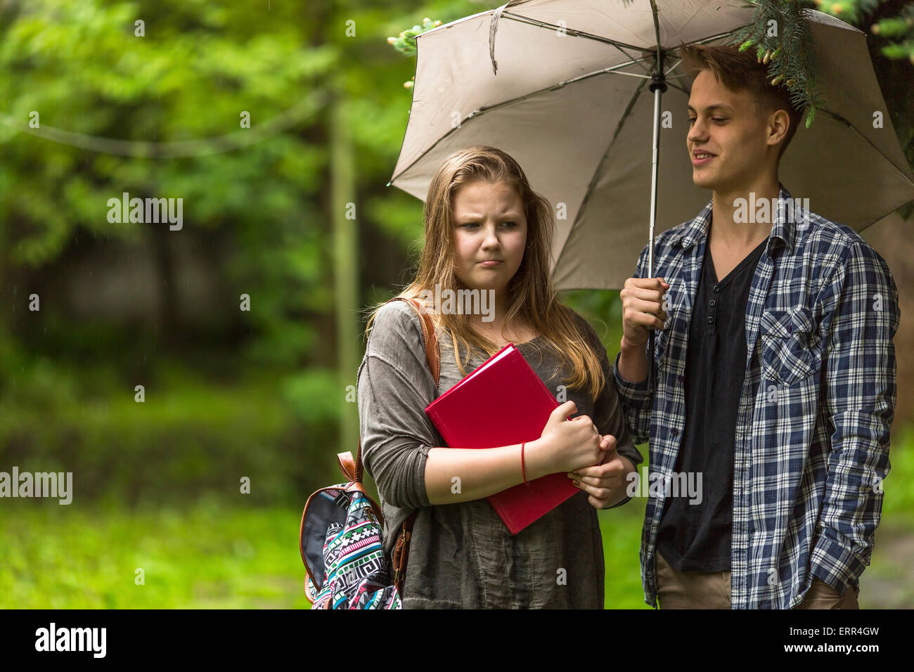 Coppia giovane di studenti ragazza con un libro e il ragazzo con l'ombrello all'esterno. Foto Stock