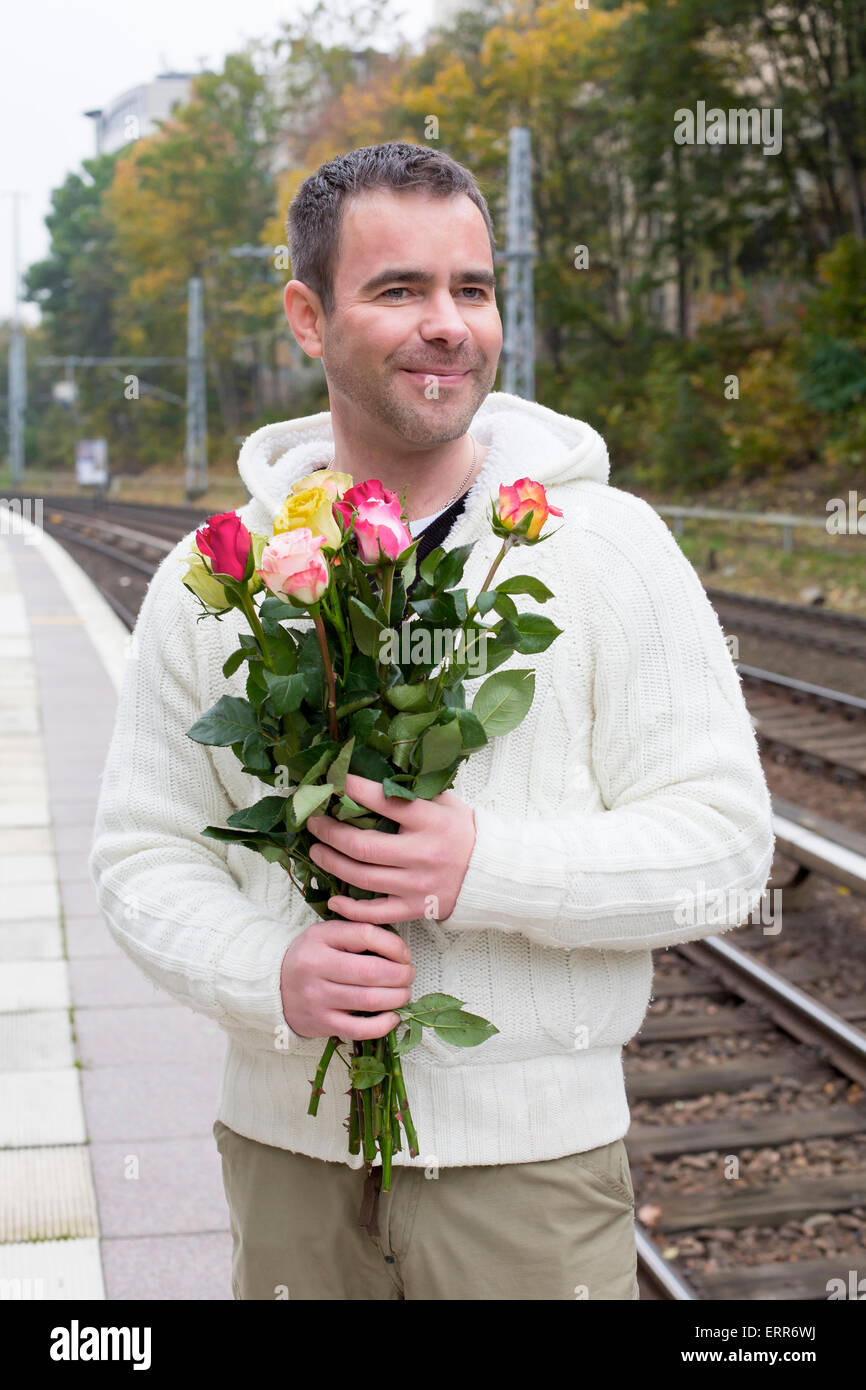 Uomo bello in attesa alla stazione ferroviaria con rose Foto Stock