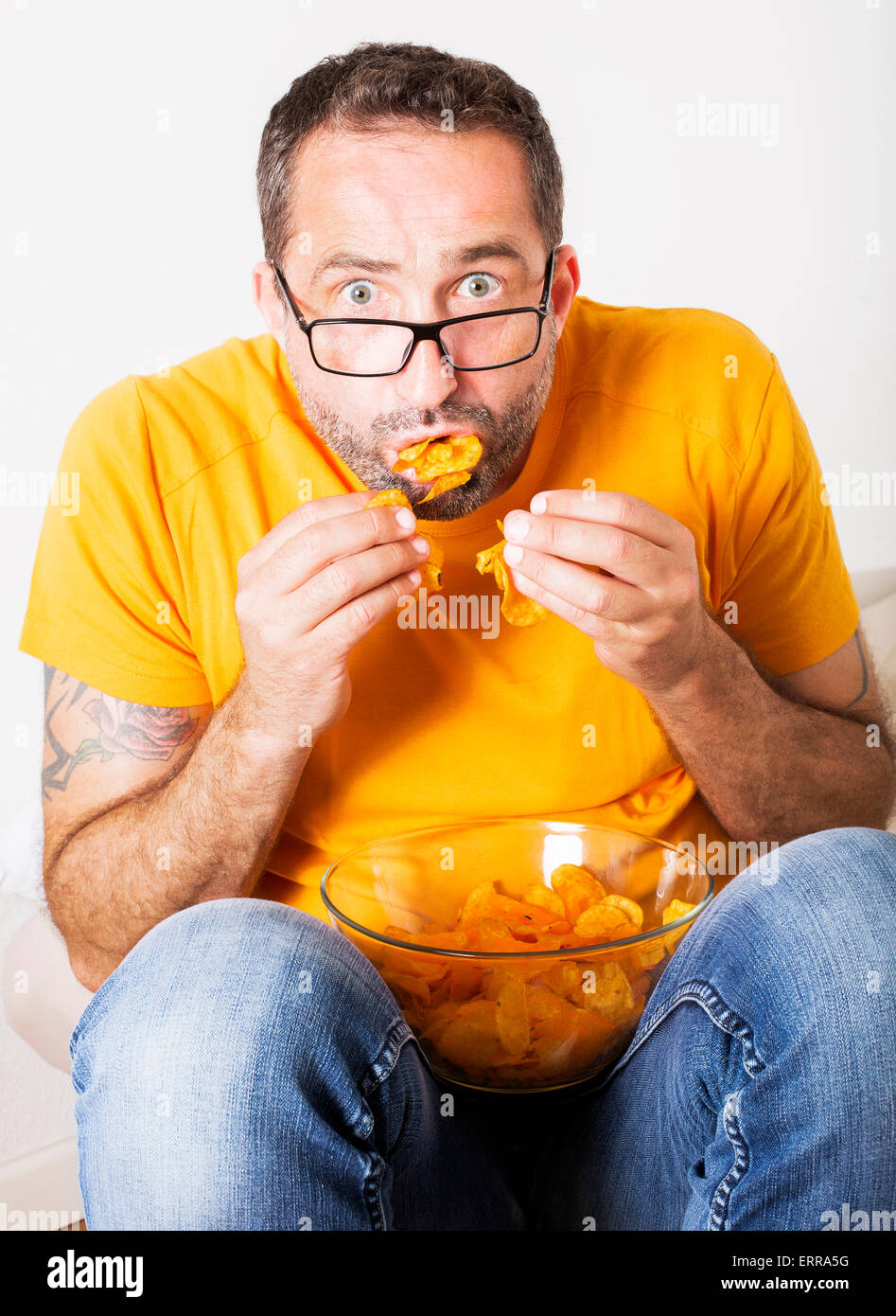 Uomo con occhiali seduto e mangiare patatine Foto Stock