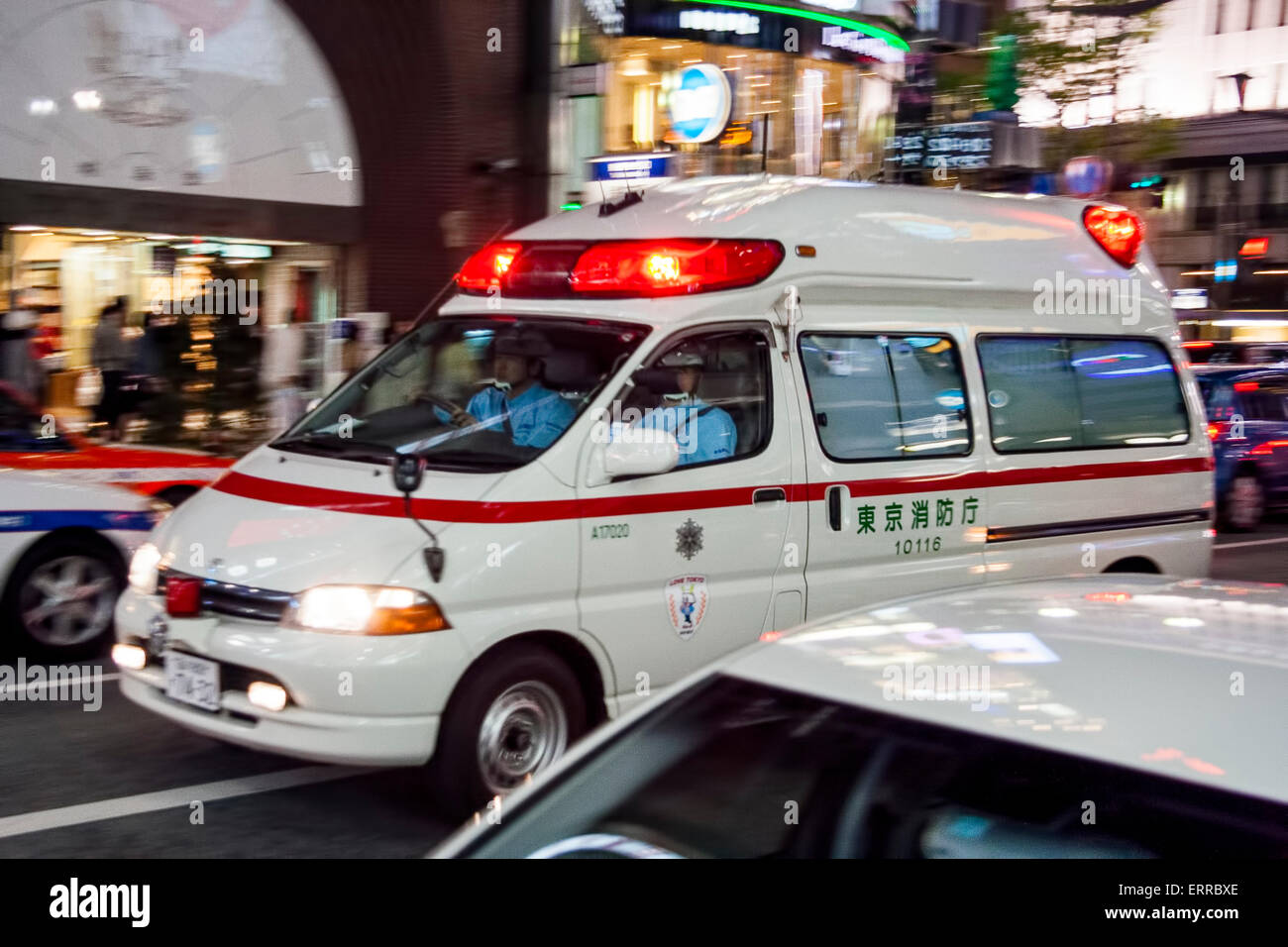 Giappone, la Ginza a Tokyo. L'ambulanza bianca che accelera il passato con le luci rosse lampeggianti, il fuoco di panning sull'ambulanza con la sfocatura di movimento sulla strada circostante. Foto Stock