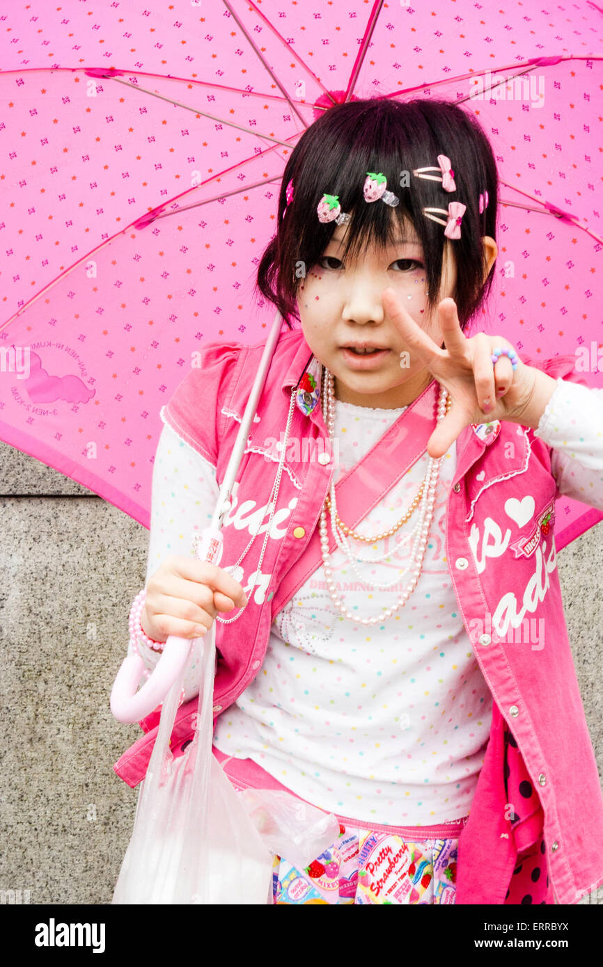 Harajuku, Toyko. Contatto visivo con una giovane donna, che dà un gesto di pace, vestito di rosa e bianco, tenendo un ombrello rosa. Stile Harajuku. Foto Stock