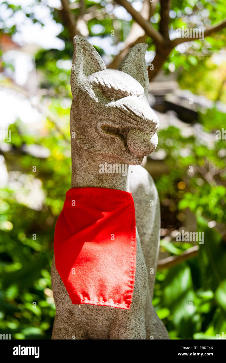 Santuario di Gosha Inari a Kobe, Giappone. Primo piano di una statua di Kitsune in pietra, testa di volpe che tiene una palla in bocca e bib rosso intorno al collo. Foto Stock