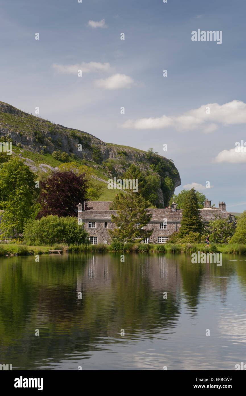 La luce del sole estivo & pittoreschi cottage in pietra stand sulle rive di un suggestivo lago di pesca, Kilnsey Crag oltre - Kilnsey Park, Yorkshire Dales, Inghilterra, Regno Unito. Foto Stock