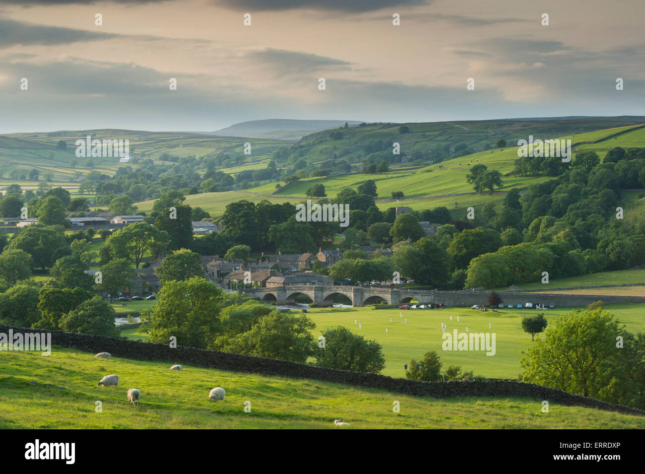 Idillio rurale - bella campagna panoramica collinare e tradizionale villaggio cricket match sulla soleggiata estate sera - Burnsall, Yorkshire Dales, Inghilterra, Regno Unito. Foto Stock