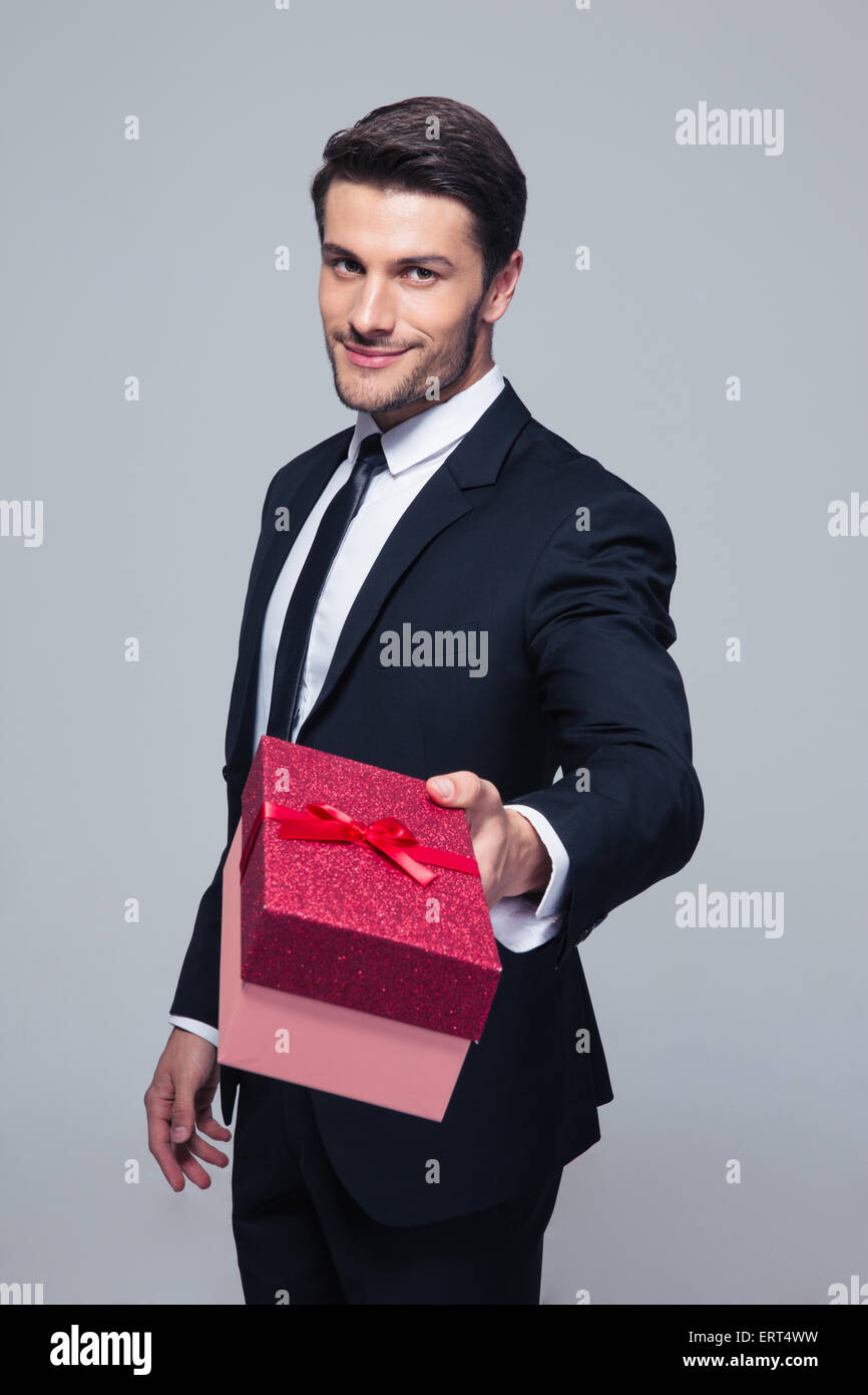 Happy businessman dando confezione regalo su telecamera su uno sfondo grigio Foto Stock