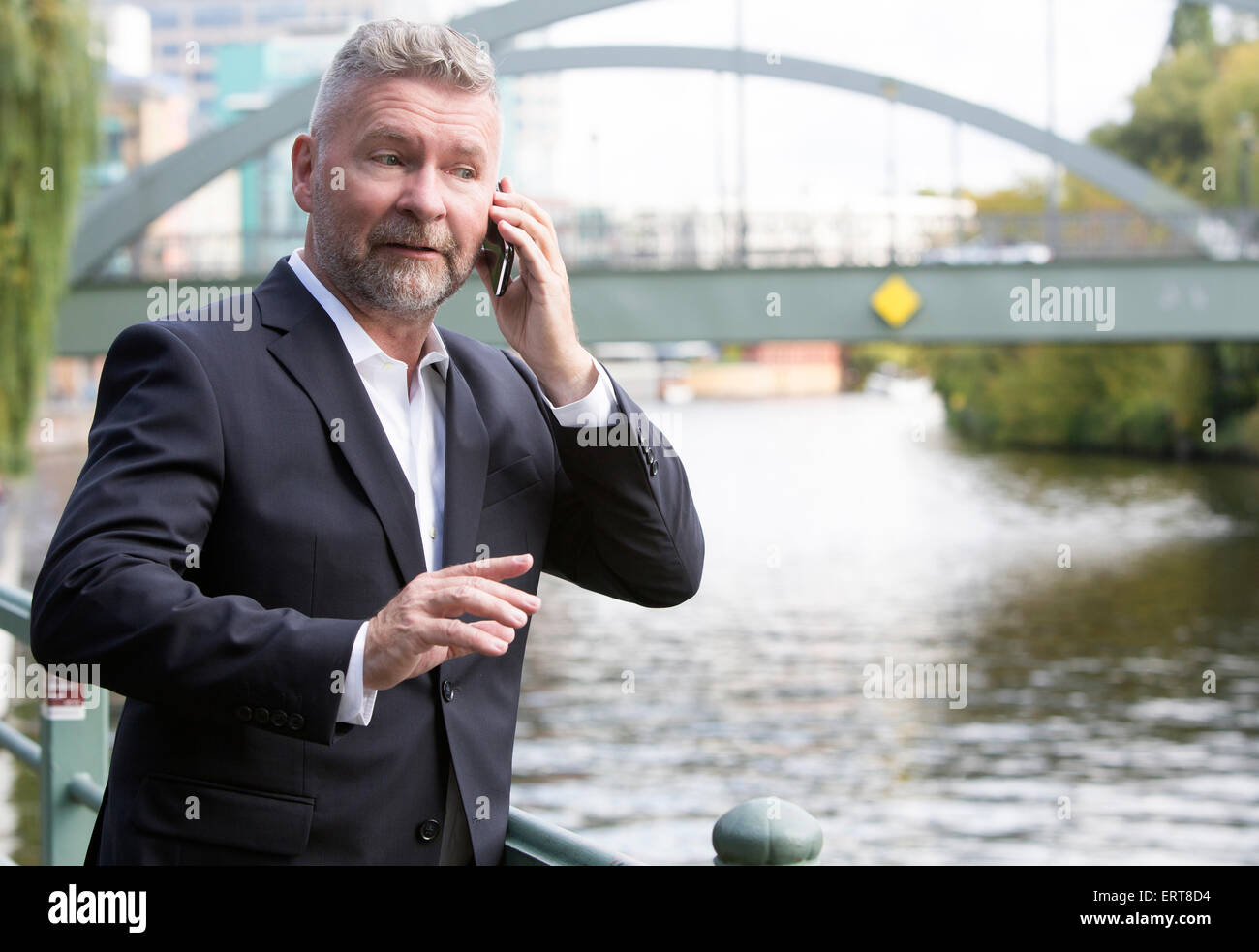 Imprenditore in un vestito in piedi di fronte a un ponte e parlando al telefono Foto Stock