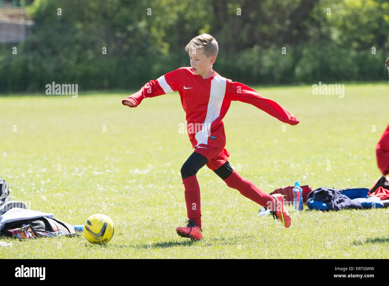 Giovane ragazzo giocando a calcio nel parco indossando la sua red kit calcio inseguendo la palla Foto Stock