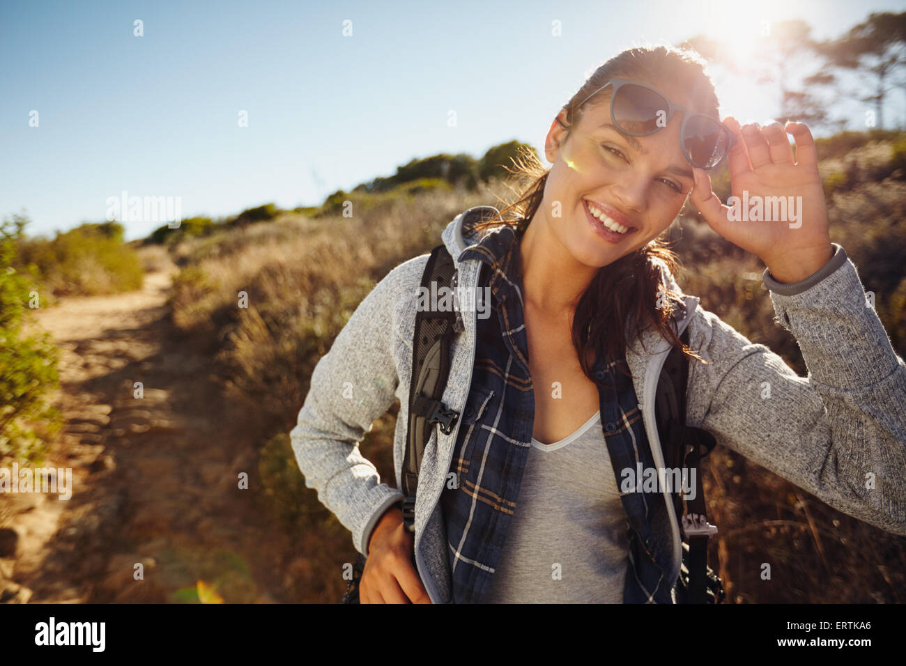 Ritratto di un giovane felice escursionista donna in natura. Giovane donna caucasica indossando occhiali da sole guardando la fotocamera con uno zaino su una Foto Stock