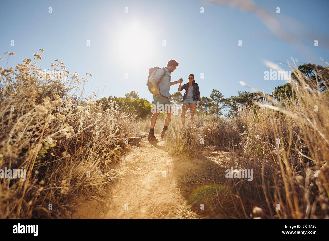 Colpo all'aperto di una giovane coppia in vacanza escursioni, passeggiate su sentiero sterrato in montagna tenendo le mani. Giovane uomo e donna escursionista su sunn Foto Stock