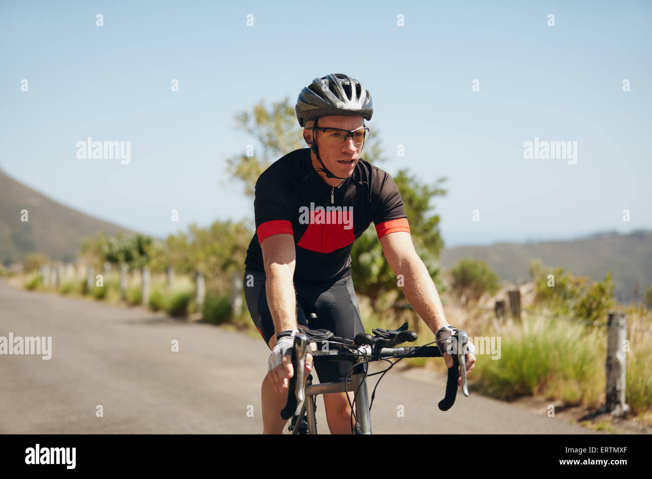 L'uomo triathlon atleta ciclista in sella in discesa sulla strada di campagna. Giovane uomo equitazione bicicletta su strada aperta, la pratica per il triathlon Foto Stock