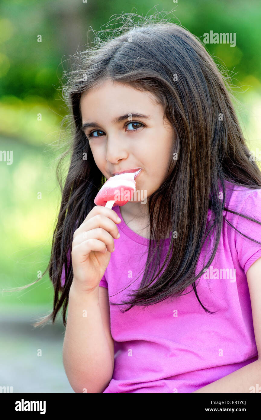 Gentile bambina godendo un congelato o per lecca-lecca il gelato guardando la telecamera Foto Stock