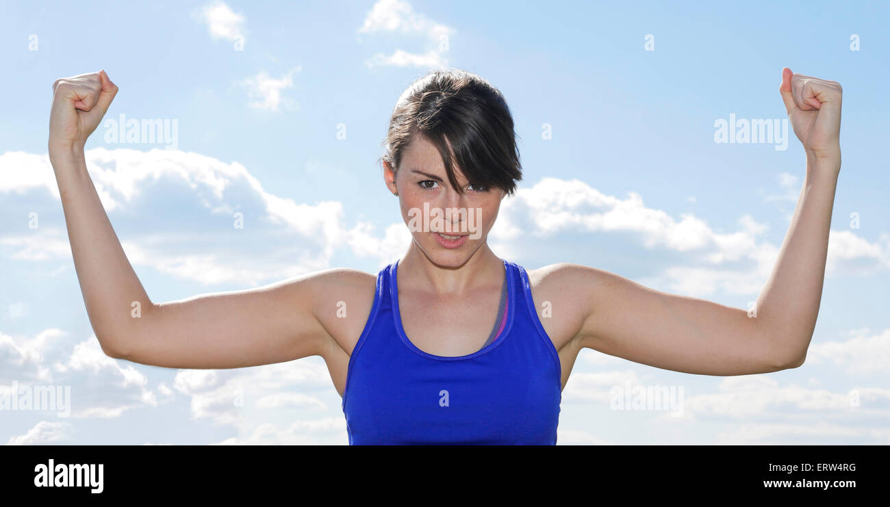 Giovane donna flettendo i suoi muscoli nella parte anteriore di un cielo blu Foto Stock