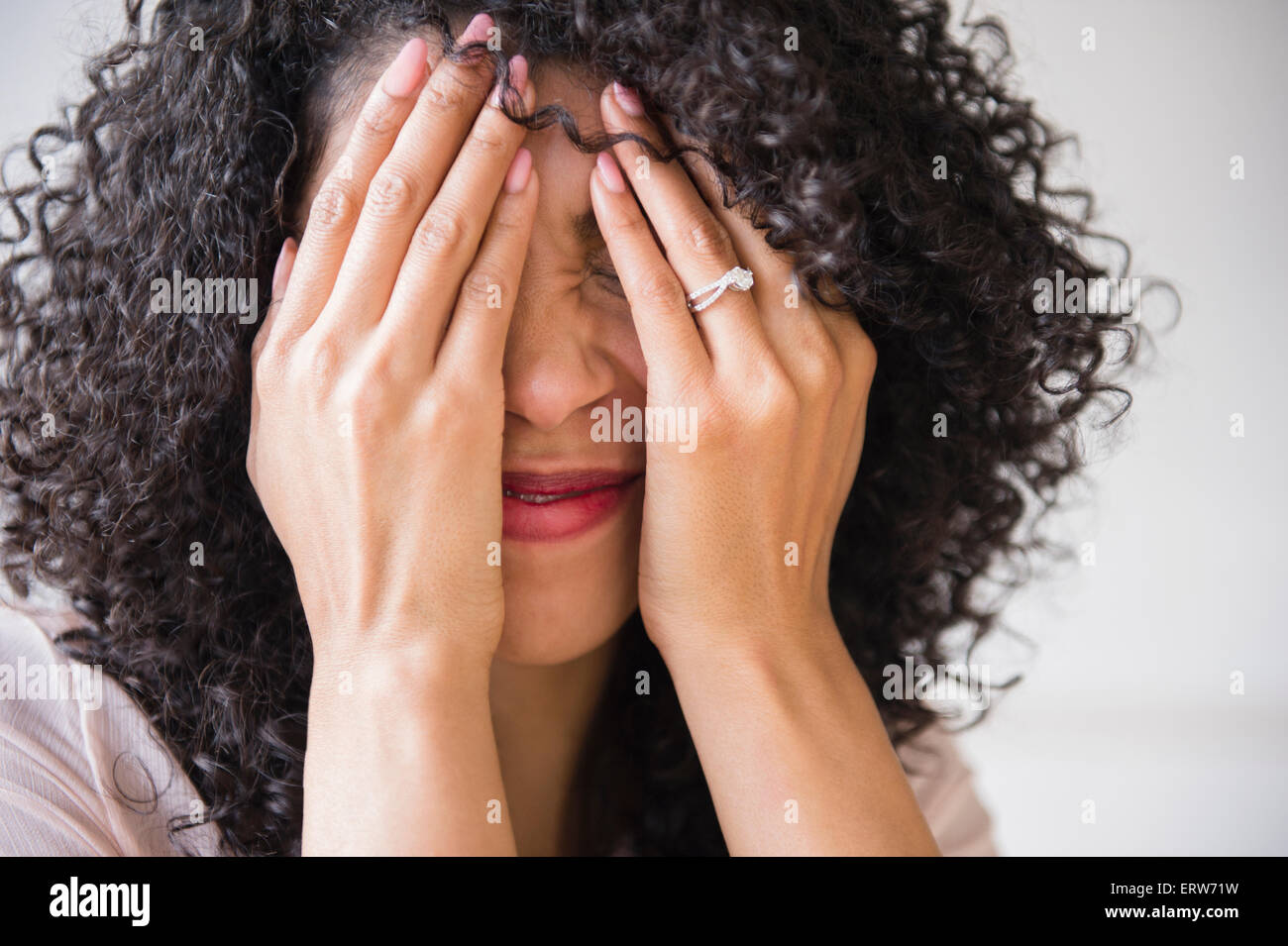 Razza mista donna con capelli ricci che copre il volto Foto Stock