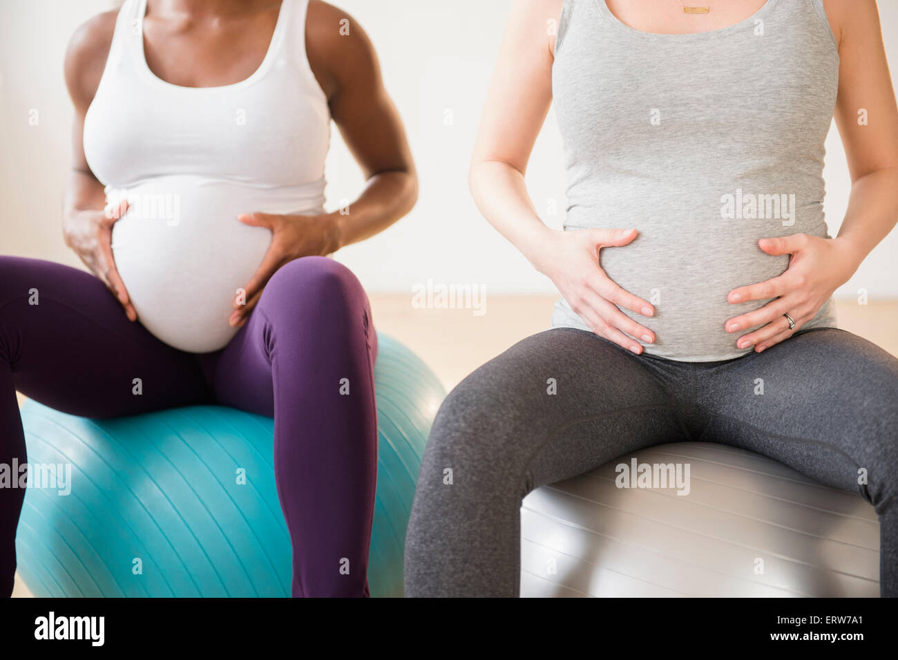 Donne in stato di gravidanza tenendo gli stomaci seduti sulle sfere di fitness Foto Stock
