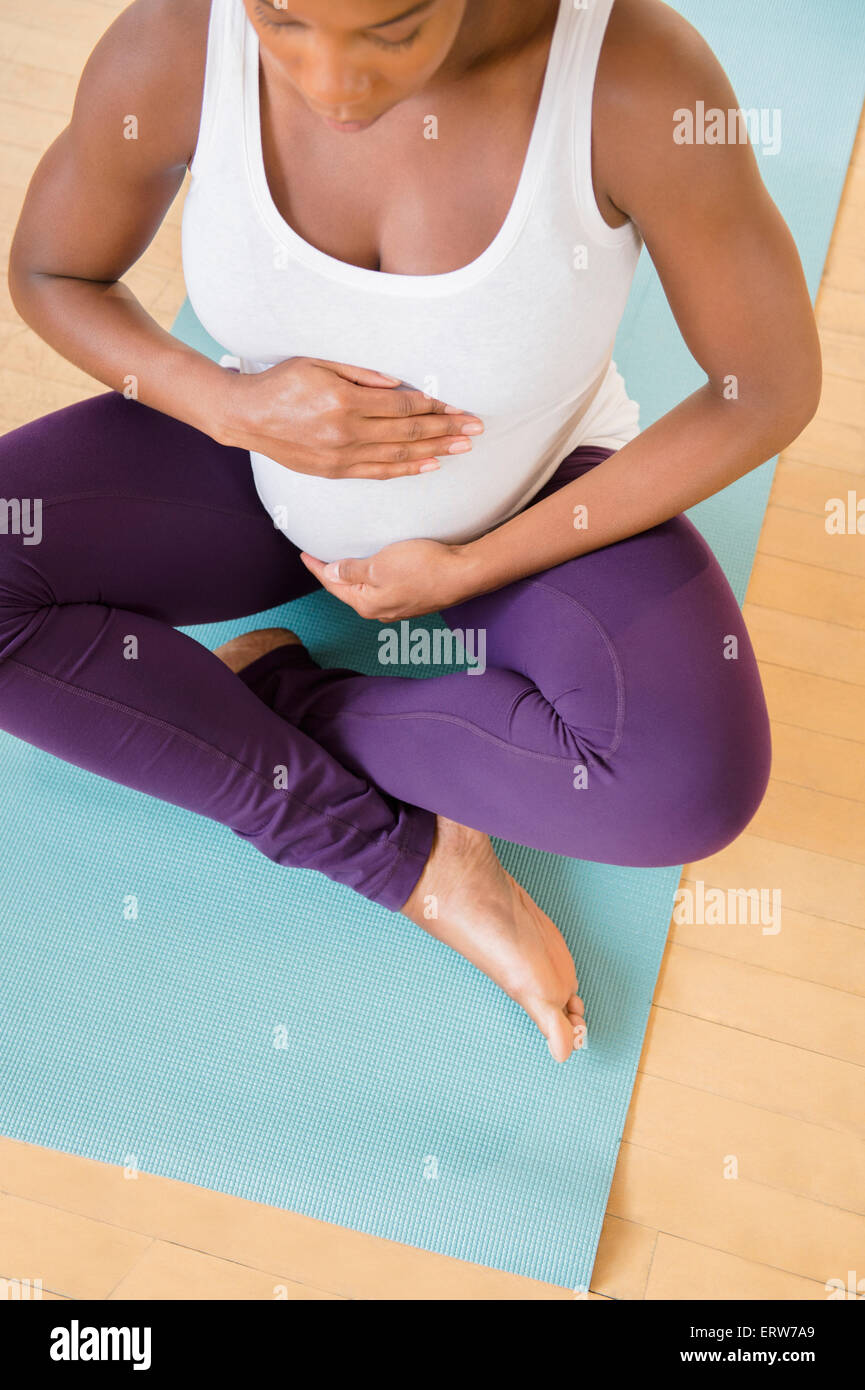 Nero donna incinta seduta sul tappetino di esercizio tenendo lo stomaco Foto Stock