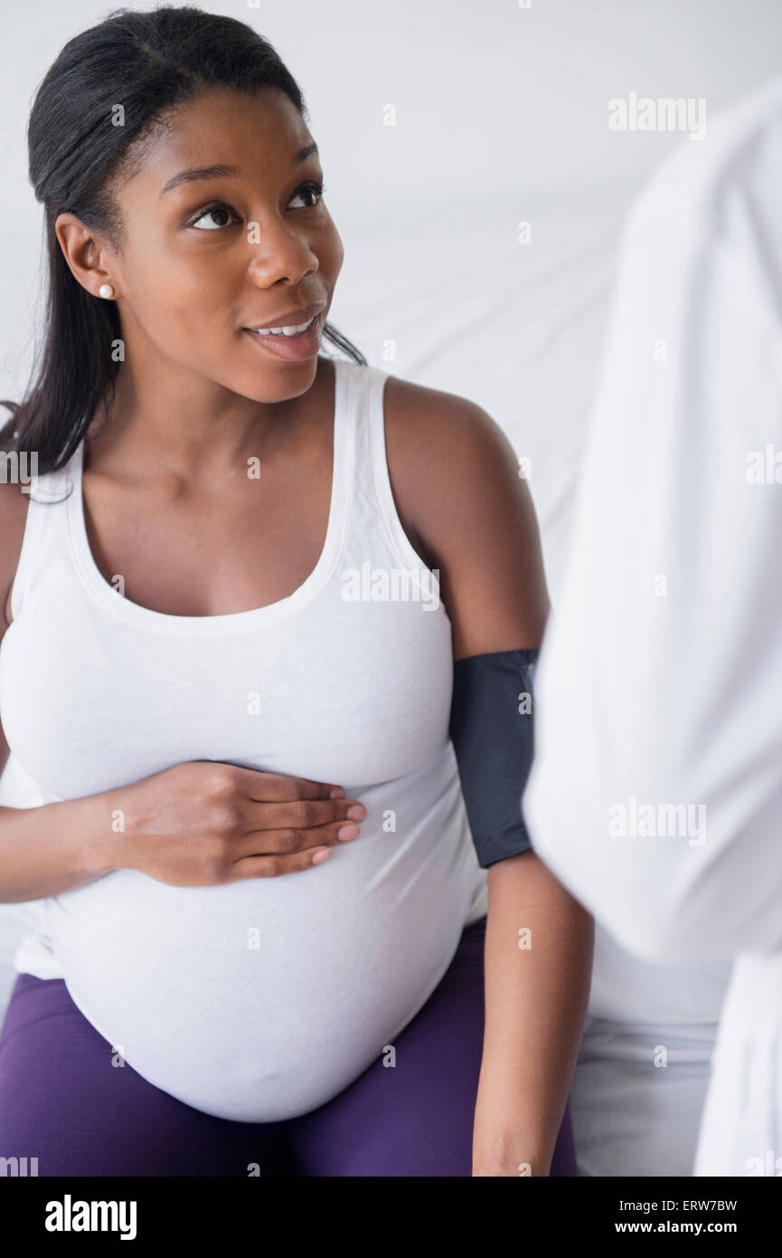 Medico controllando la pressione del sangue nero della donna in stato di gravidanza Foto Stock