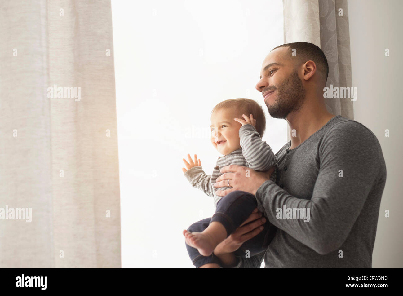 Sorridente padre e figlio bambino a guardare fuori dalla finestra Foto Stock