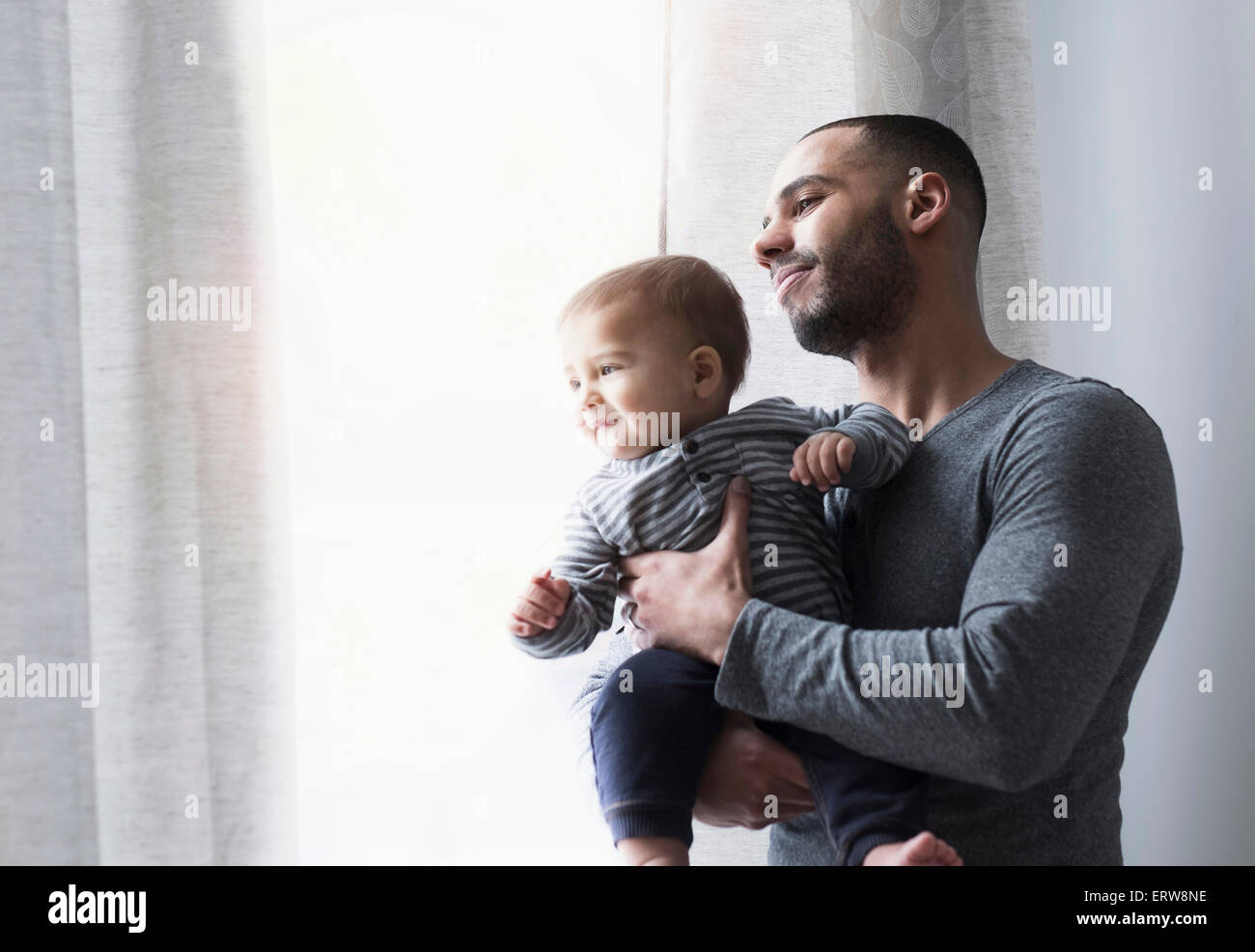 Sorridente padre e figlio bambino a guardare fuori dalla finestra Foto Stock