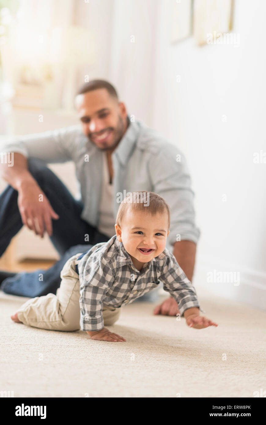 Padre guardando baby figlio di strisciare sul pavimento Foto Stock