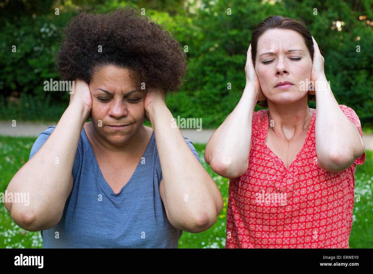 Due donne nel parco che copre le sue orecchie e chiudendo gli occhi Foto Stock
