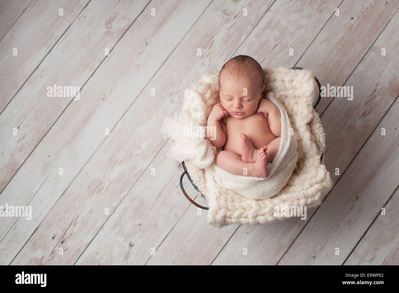 Un ritratto di sette giorni di età, neonato dorme in un cestello in filo metallico su un dipinto di bianco, con pavimento in legno. Foto Stock