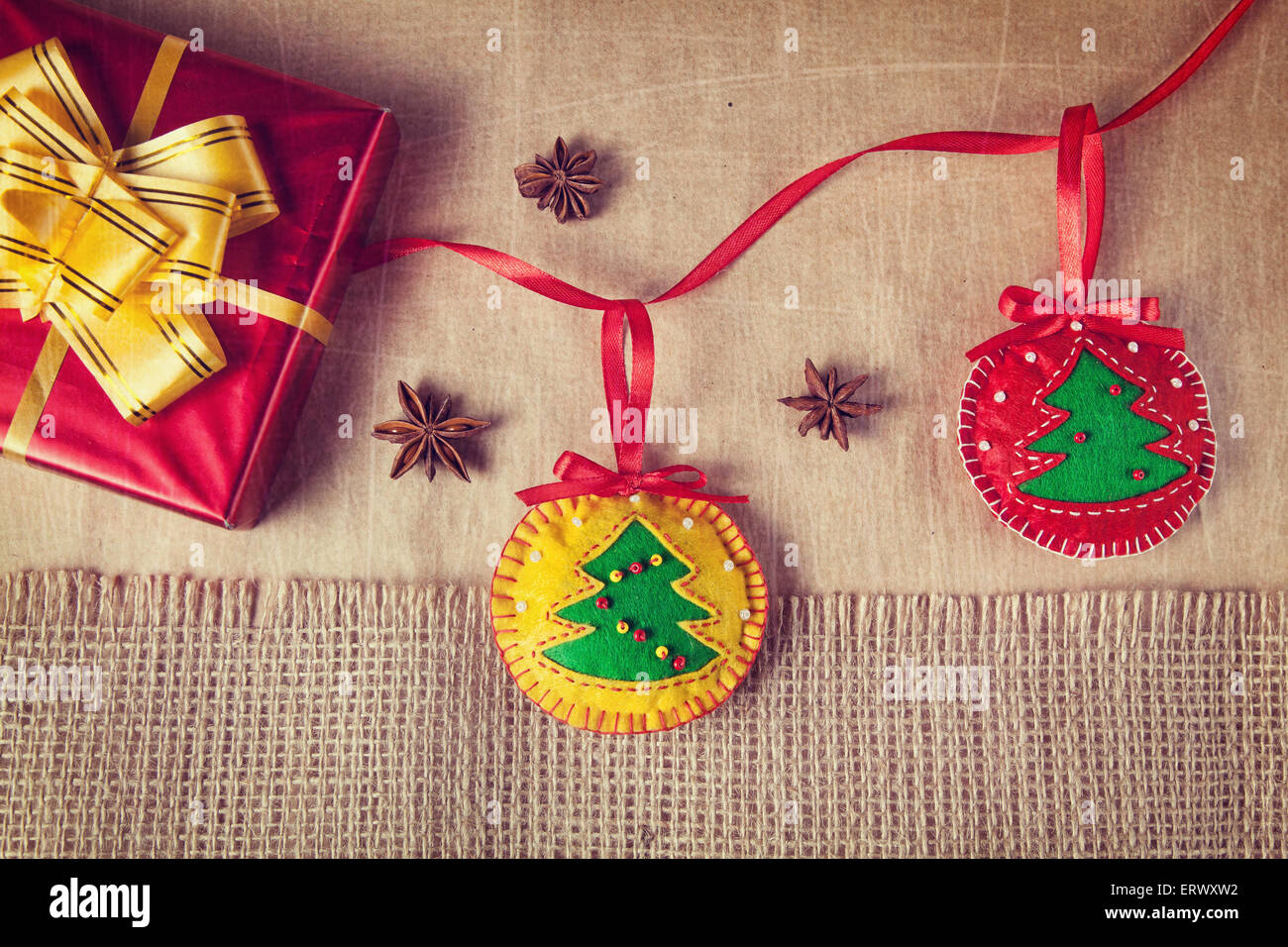 Natale giocattoli fatti a mano dal feltro, casella rossa con prua giallo e anice stelle intorno sulla carta e il cilicio sfondo Foto Stock