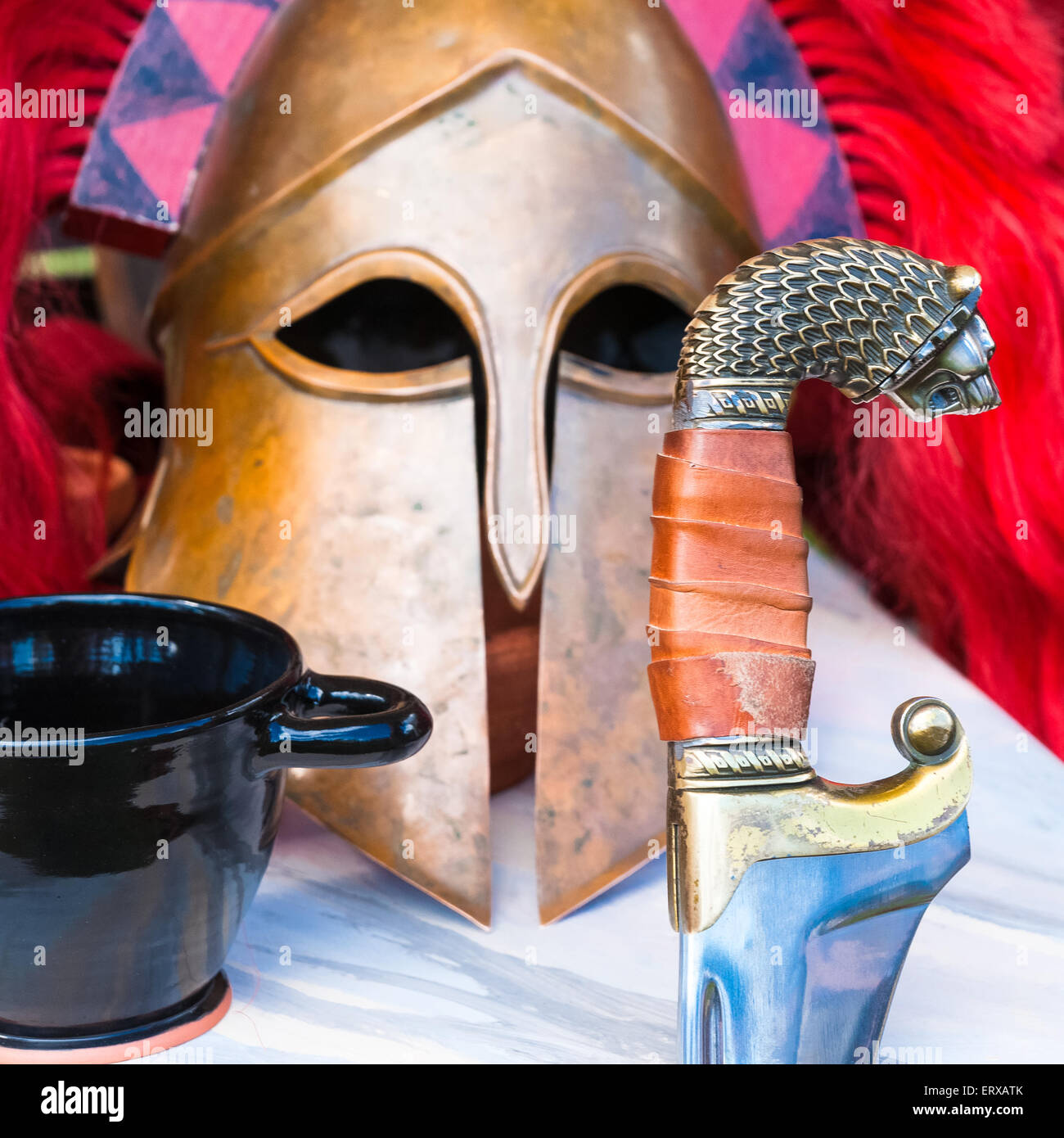 Spartan still-life di una spada, un elmetto militare e un bicchiere di vino su una tavola. Fotografia quadrata Foto Stock