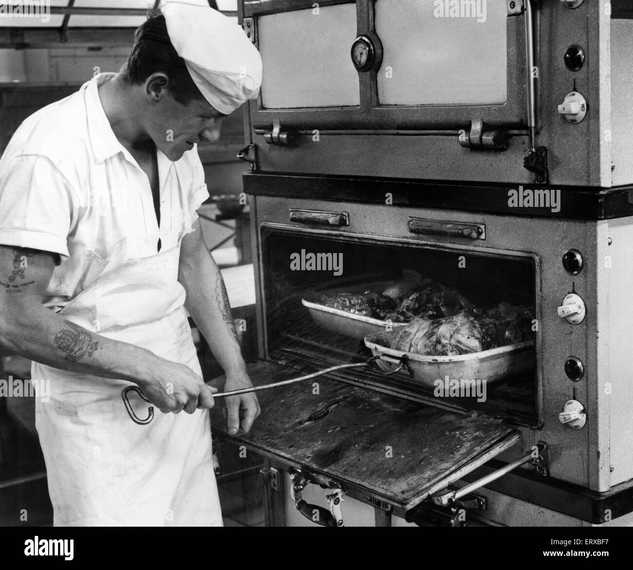 RAF Brawdy, Pembrokeshire, Galles. Il 14 luglio 1962. Cuocere J Green controlli sull'arrosto di agnello cottura in Brawdy Stazione di aria nel condotto. Foto Stock