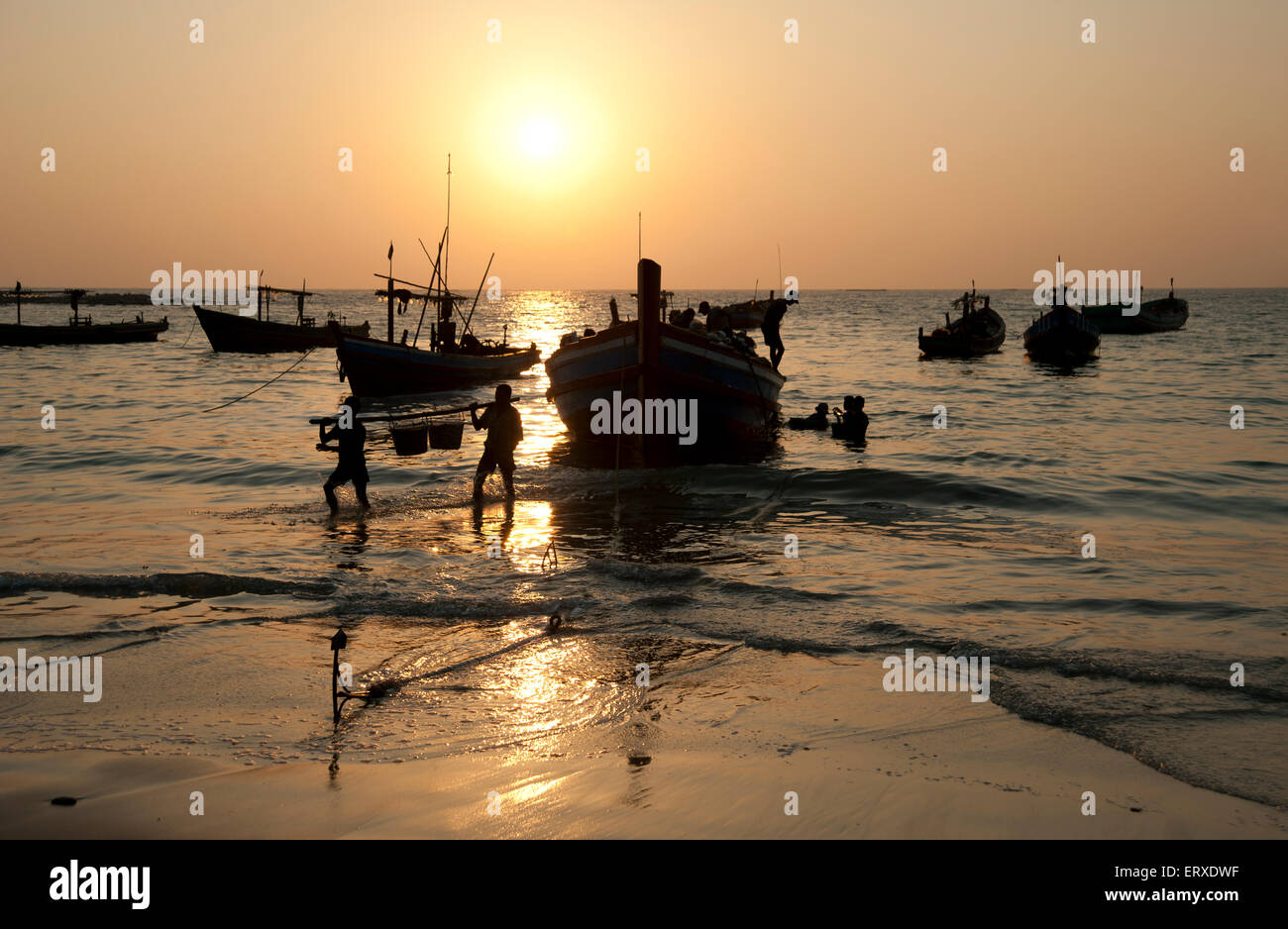 Sagome di pescatori birmani off caricando le loro barche al tramonto sulla spiaggia di Ngapali Myanmar Foto Stock