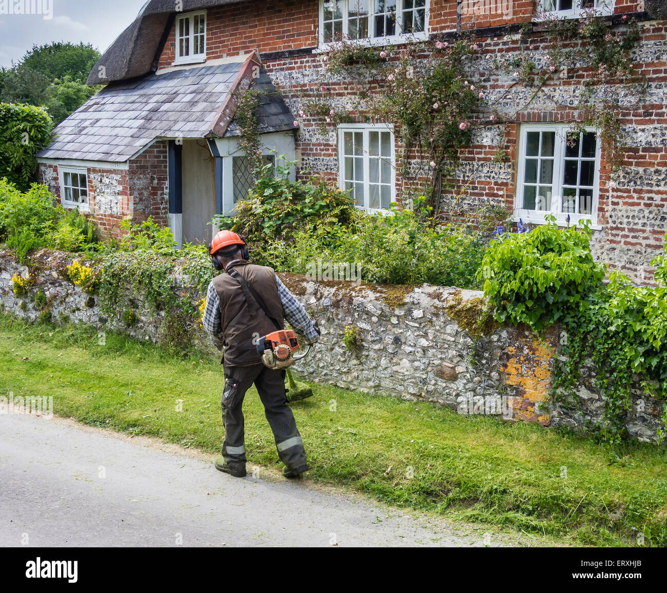 Uomo con decespugliatore nel villaggio di Martin, Hampshire, Inghilterra, Regno Unito Foto Stock