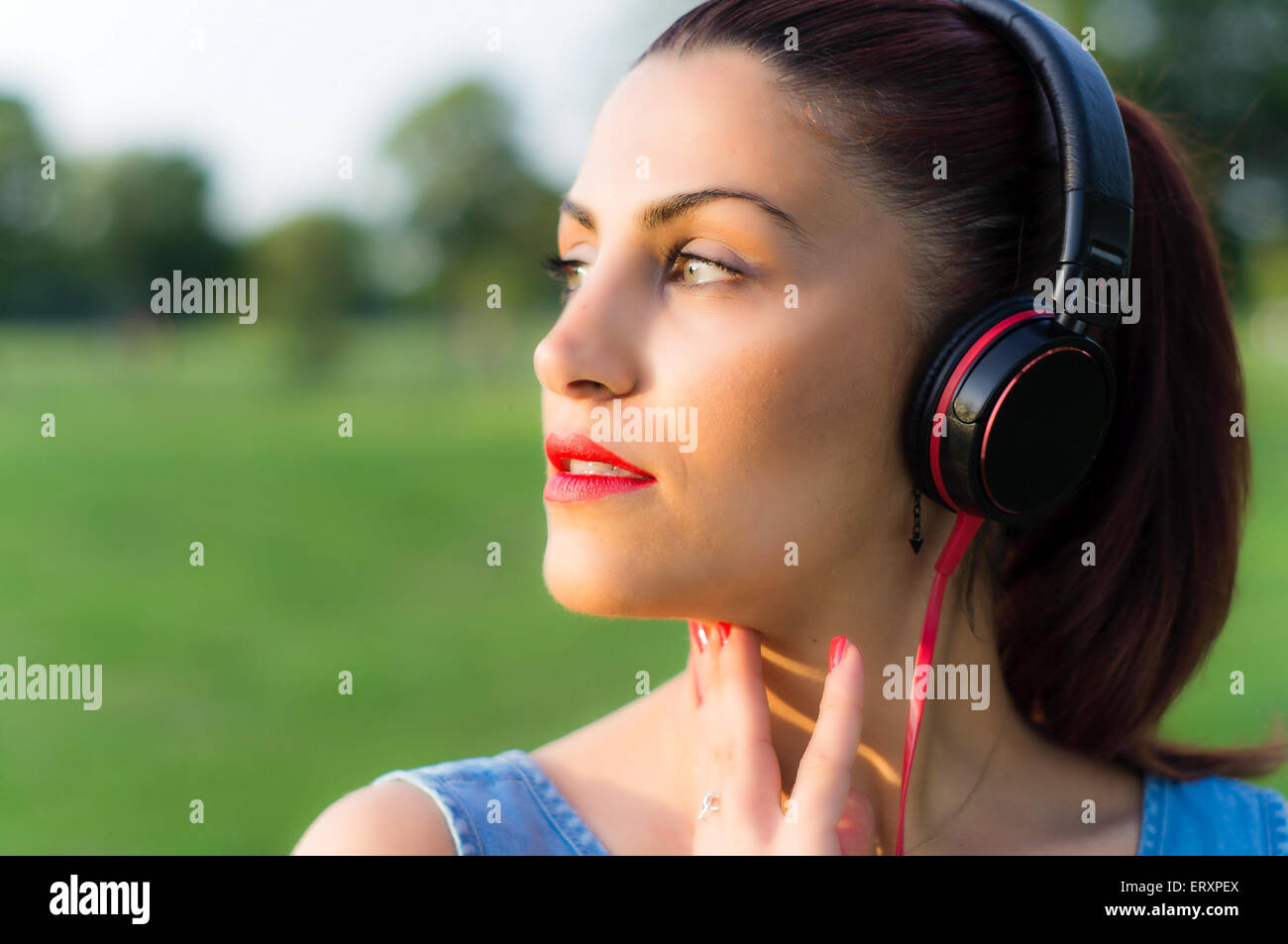 Bella giovane donna ascoltando la musica attraverso le cuffie in un parco vicino fino Foto Stock