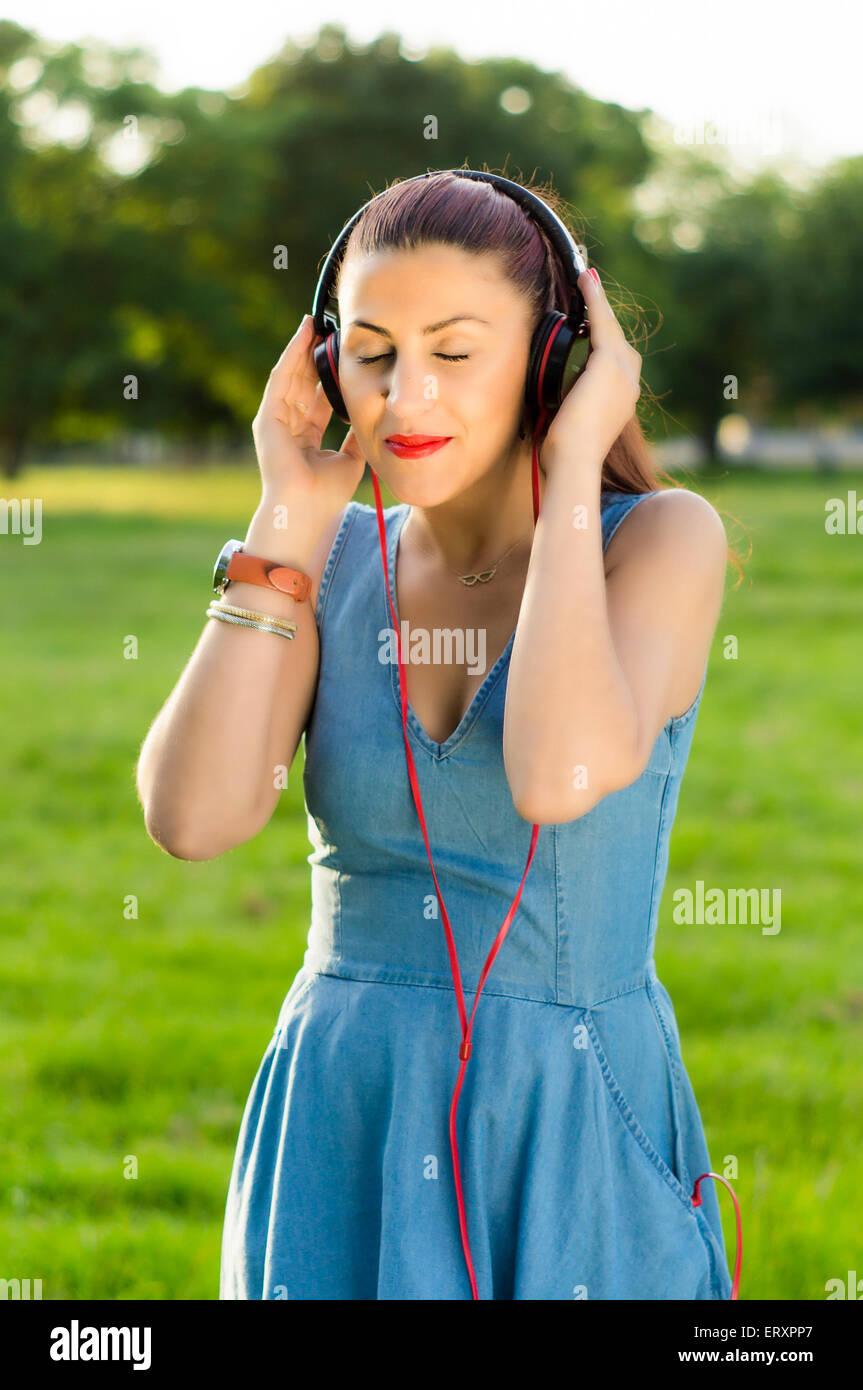 Bella Donna con le cuffie per ascoltare musica occhi chiusi oltre il parco di alberi di sfondo all'aperto Foto Stock