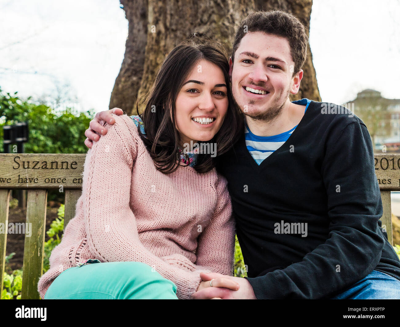Romantico Coppia giovane seduto su una panchina nel parco insieme e sorridente guardando la telecamera Foto Stock
